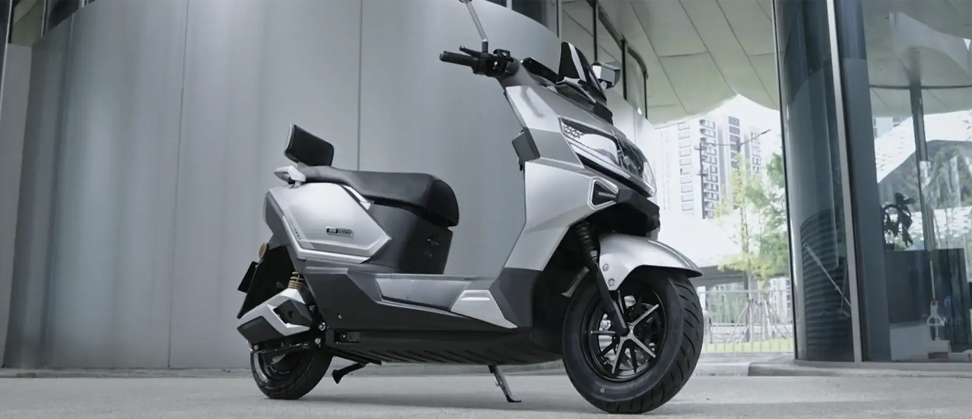 A sleek silver electric scooter parked outside a modern building, showcasing innovative transportation technology suitable for city commuting.
