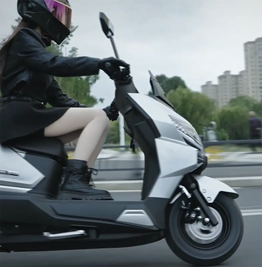Person riding a modern electric scooter wearing a helmet and stylish outfit, commuting through an urban area with high-rise buildings in the background.