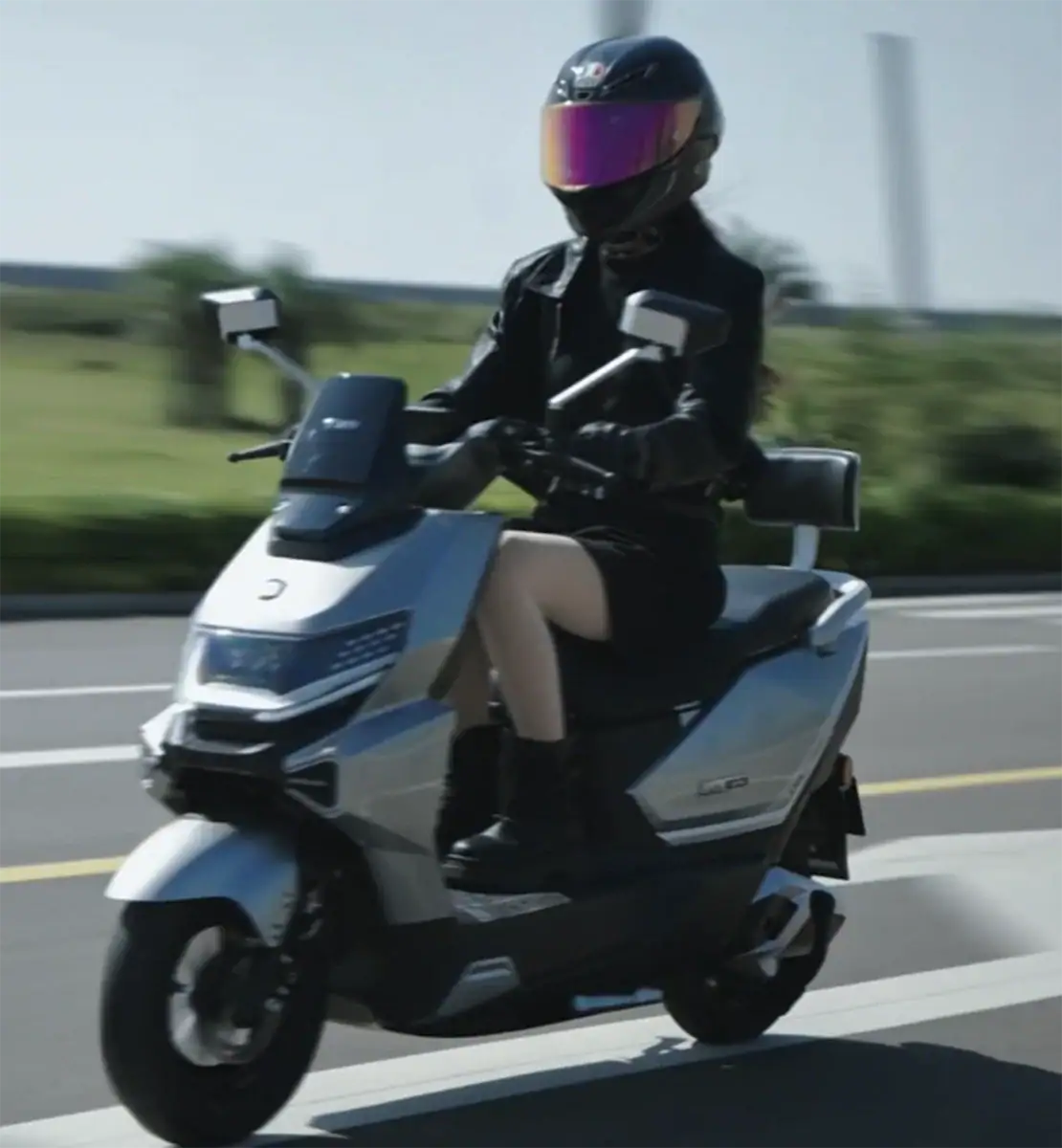 A woman riding a sleek electric scooter wearing a black helmet and black gear, driving fast on the street, showcasing modern personal transportation technology.